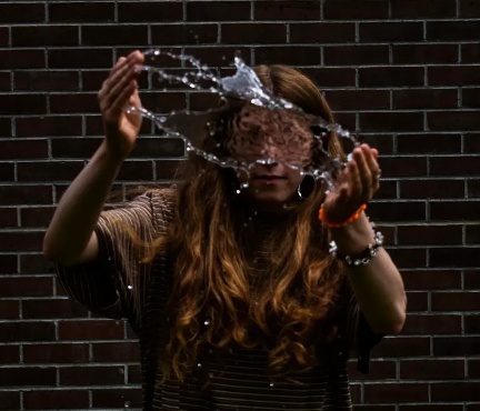 A splash of water caught in front of a face, against a brick wall