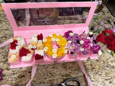 A flower arrangement in a pink box, spelling MOM