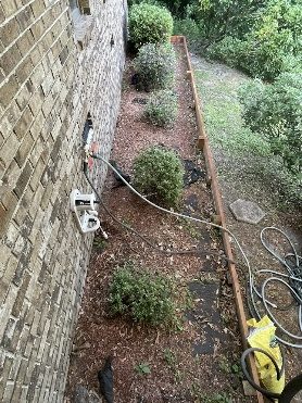 A narrow bed along a brick wall with a hose, mid-job
